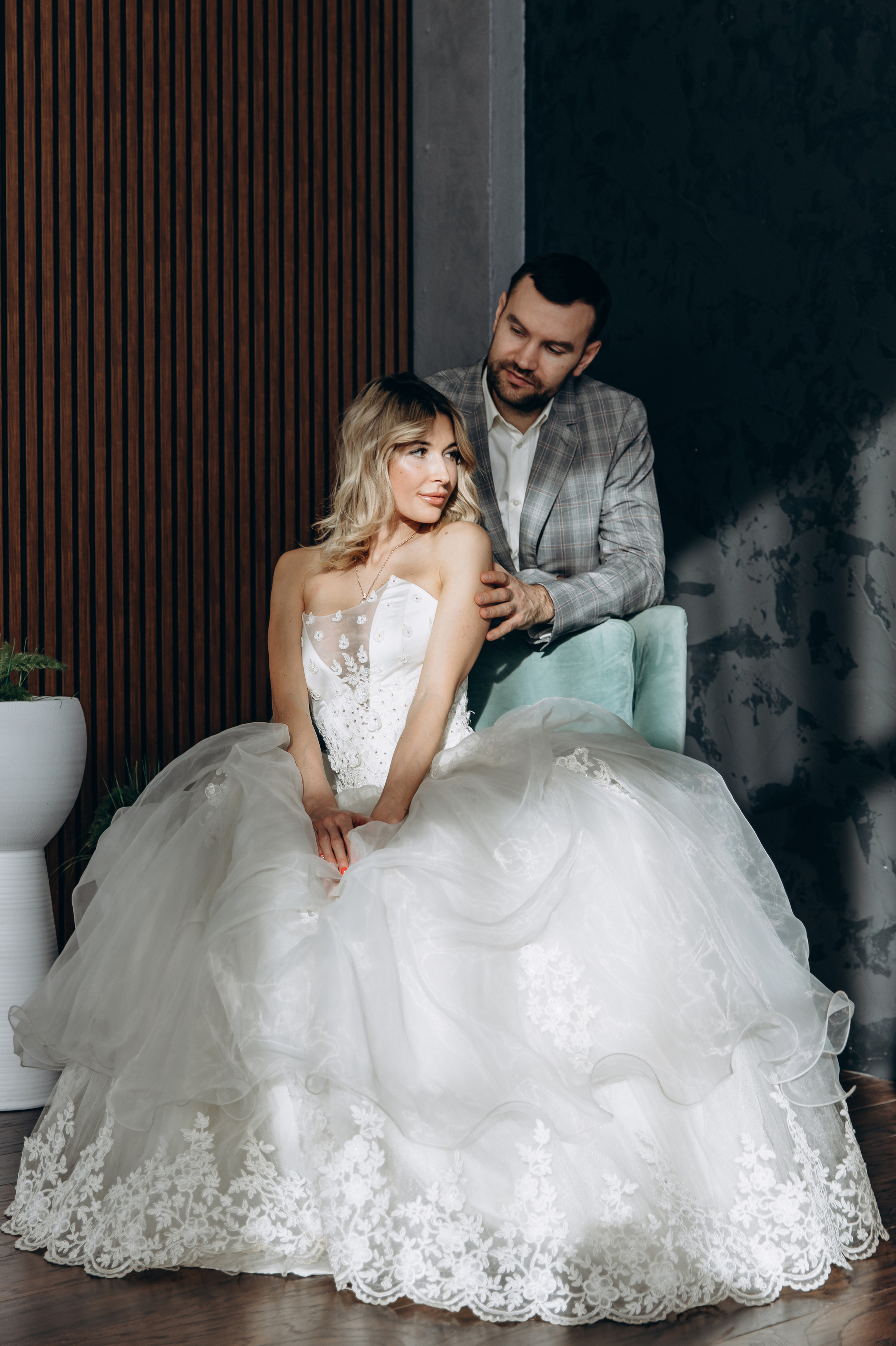 The bride sits on a chair, the groom hugs her from behind